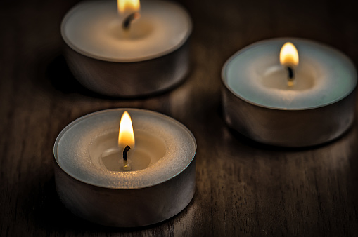 Three burning round candles on wooden table
