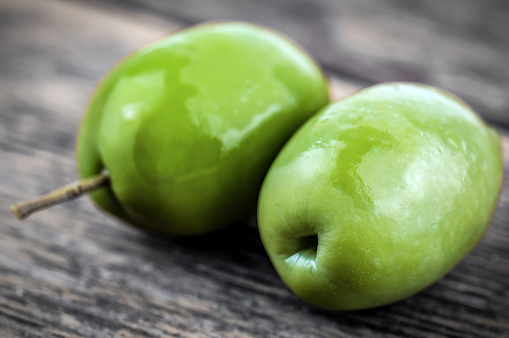 Two green delicious olives on wooden background