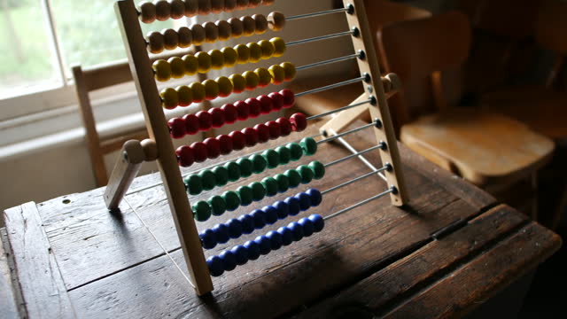 Brightly colored abacus on aged wooden desk, a symbol of traditional education and arithmetic. Essential for themes involving learning, counting, and historical teaching methods