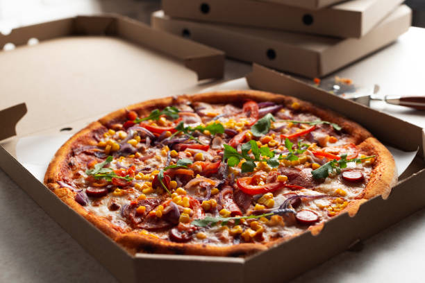 istock Large Pizza in open carton box and cutter on kitchen table closeup view 2149102210