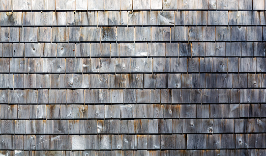 Wide view of several rows of weathered and grayed cedar shingles in the morning light.