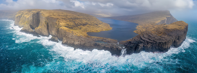 Trælanípa and Lake Leitisvatn, Vágar, Faroe Islands: Trælanípa  is a rock wall, which juts 142 metres upwards out of the sea. I

Lake Leitisvatn is the largest lake in the Faroe Islands. The lake has also been named “the lake over the ocean” as the view from Trælanípan from a particular angle functions as an optical illusion, appearing to look as though the lake is hovering directly above the ocean. 

At the end of the lake is the impressive Bøsdalafossur waterfall. Bøsdalafossur is a 30m high waterfall flowing directly into the Atlantic Ocean.