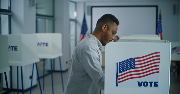 African American man takes paper ballot for voting from polling officer at polling station. US citizen walks to voting booth to fill bulletin. Election Day in the United States of America. Civic duty.