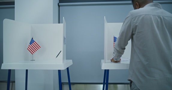 Dolly shot of diverse American citizens voting in booths in polling station office. National Election Day in the United States. Political races of US presidential candidates. Concept of civic duty.