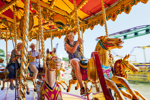 Senior adults visiting an outdoor travelling carnival in the North East of England. They are riding a carousel together.\n\nVideos are available similar to this scenario.