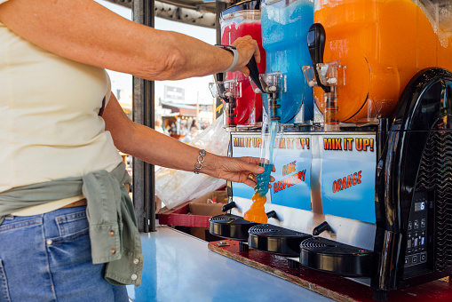 Close up of an unrecognisable senior woman making a slushie drink while visiting an outdoor travelling carnival. She is putting different coloured ice slush into a cup. The fairground is in the North East of England.

Videos are available similar to this scenario.