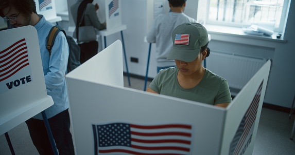 Female American soldier comes to vote in booth in polling station office. National Election Day in the United States. Political races of US presidential candidates. Concept of civic duty. Dolly shot.