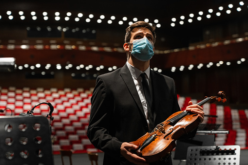 Worried musician standing on a stage holding an instrument wearing a protective face mask