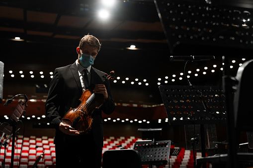 Front view of a solo violinist standing on the stage in an empty theater holding an instrument