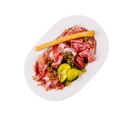 Top view of a selection of italian meats and pickles served on a white plate, isolated on white background