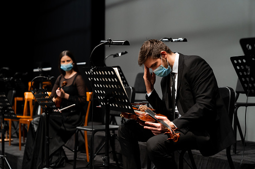 Rear view of two musicians playing instruments together on a stage wearing a protective face mask