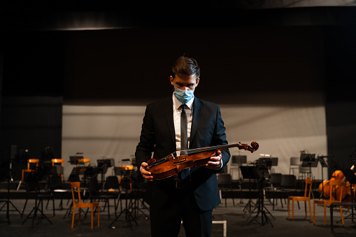 Portrait of a musician standing on a stage holding an instrument with a protective face mask on