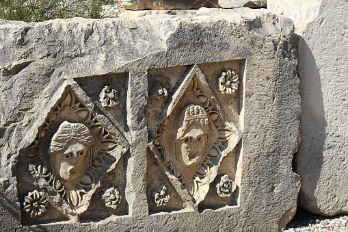Historical stone bas-relief with carved faces in ancient city of Myra on sunny day. Dead civilization. Ruins of rock tombs in Lycia region, Demre, Antalya, Turkiye