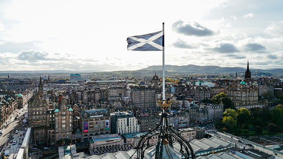 Aerial view of Edinburgh old town, aerial view of the scottish flag in Edinburgh, Edinburgh city centre, Gothic Revival architecture in Scotland, Flag of Scotland in Edinburgh\n\nEdinburgh is the capital city of Scotland and one of its 32 council areas. The city is located in south-east Scotland, and is bounded to the north by the Firth of Forth estuary and to the south by the Pentland Hills. Edinburgh had a population of 506,520 in mid-2020, making it the second-most populous city in Scotland and the seventh-most populous in the United Kingdom.\n\nThe flag of Scotland is the national flag of Scotland, which consists of a white saltire defacing a blue field.