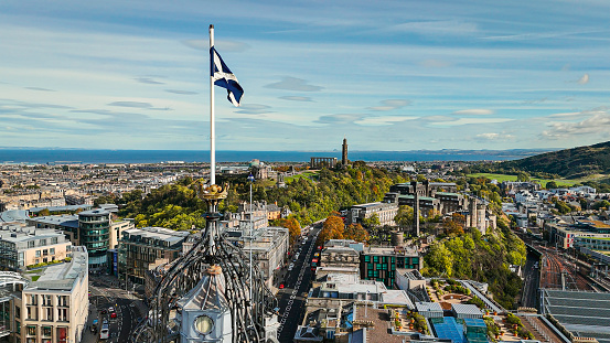 Aerial view of Edinburgh old town, aerial view of the scottish flag in Edinburgh, Edinburgh city centre, Gothic Revival architecture in Scotland, Flag of Scotland in Edinburgh\n\nEdinburgh is the capital city of Scotland and one of its 32 council areas. The city is located in south-east Scotland, and is bounded to the north by the Firth of Forth estuary and to the south by the Pentland Hills. Edinburgh had a population of 506,520 in mid-2020, making it the second-most populous city in Scotland and the seventh-most populous in the United Kingdom.\n\nThe flag of Scotland is the national flag of Scotland, which consists of a white saltire defacing a blue field.