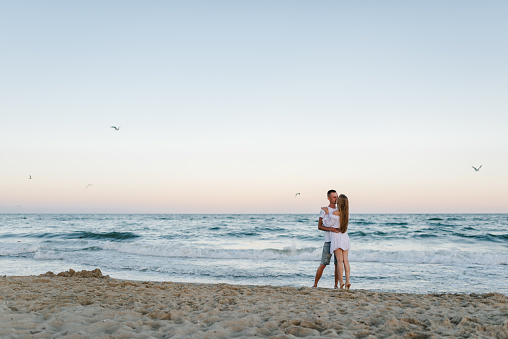 Man embraces woman walking on sand sea. Couple in love hugging and kissing on seashore. Female kisses and hugs male standing barefoot on beach with big waves ocean and enjoying a sunny summer day.