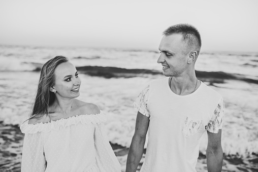 Black white photo. Happy couple in love holding hands and looking at each other walking on seashore. Female and male on beach ocean and enjoy. Man and woman walk on sand sea. Spending time together