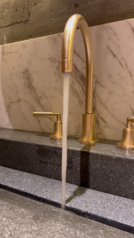 Tap water faucet in gold color: a powerful water pressure pours. Turned on the tap: a jet of water with a powerful pressure pours from tap. Accessories for the bathroom: a metallic golden faucet