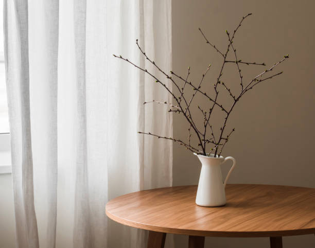 istock An enameled jug with spring branches on a round wooden table. Minimalism style decor 2149112808