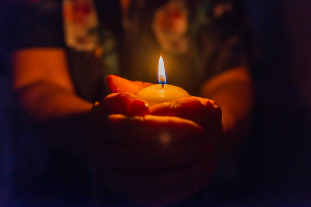 istock Candle in female hands on black dark background.Prayers candle in hands. 2149115220