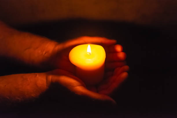 istock Burning candle in a mans hand religion concept.Candle in hands on a dark background. 2149116251