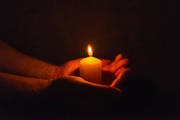 istock Burning candle in a mans hand religion concept.Candle in hands on a dark background. 2149116270