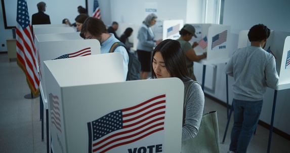 Asian woman comes to vote in booth in polling station office. National Election Day in the United States. Political races of US presidential candidates. Concept of civic duty. Slow motion. Dolly shot.