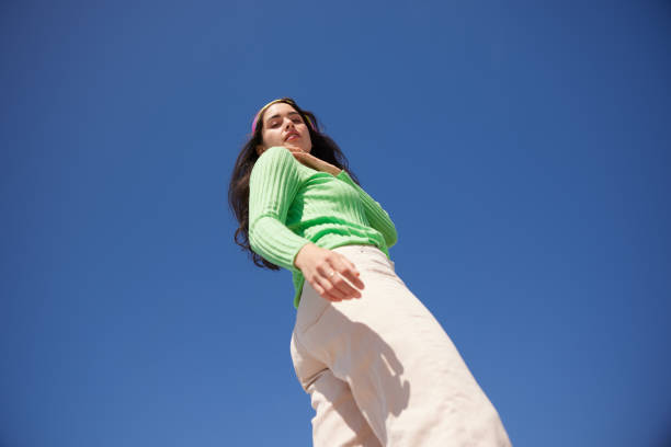 Outdoors, a young woman engages in a dynamic, dance-like body gesture, her colorful clothing adding to the vibrancy of the scene. Captured from a wide-angle, low angle view.