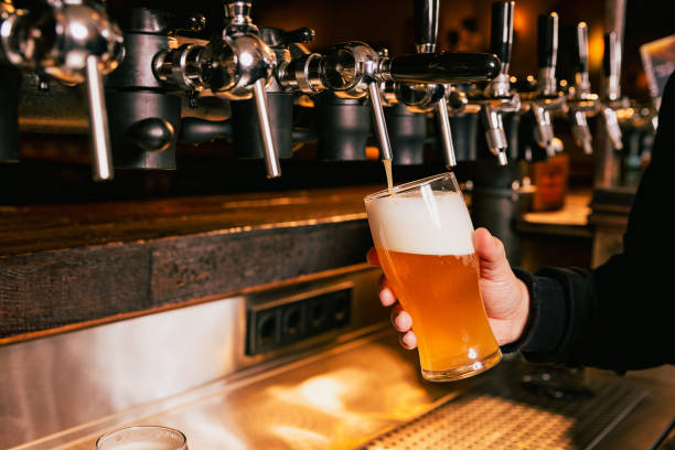 istock Bartender pouring light, cold foamy beer from tap into glass at bar with multiple beer dispensers. Serving craft beer from tap. Beer Fest concept. 2149119636
