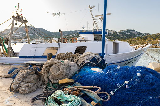 Puerto Andratx, Spain -April 14, 2024:  Fishing nets and a fishing boat in the harbor of Andratx in the late evening sun. The harbor in Puerto Andratx, Mallorca, is renowned for its affluent international visitors, whether tourists or residents, especially during sunset and for its pub nightlife.
