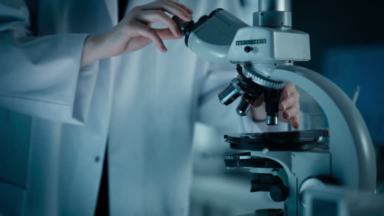 Two Laboratory Technicians Examining Microscopic Cells Through a Modern Microscope. Close Up of Anonymous Scientists Conducting Medical Research and Discovery in Science Facility