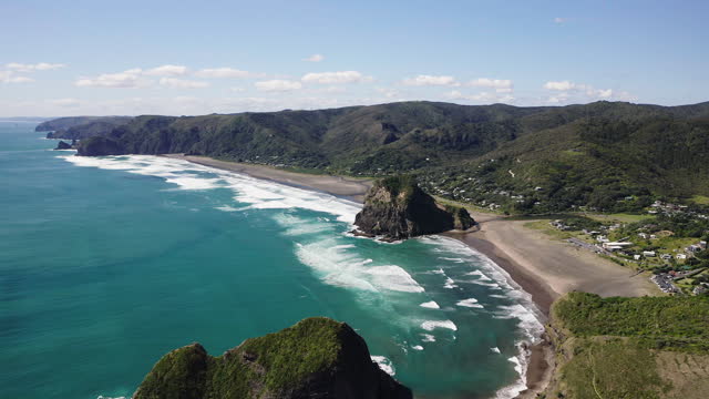 Passing over one of the two rocky outcrops on the stunning Piha Beach, New Zealand on the Tasman Sea.