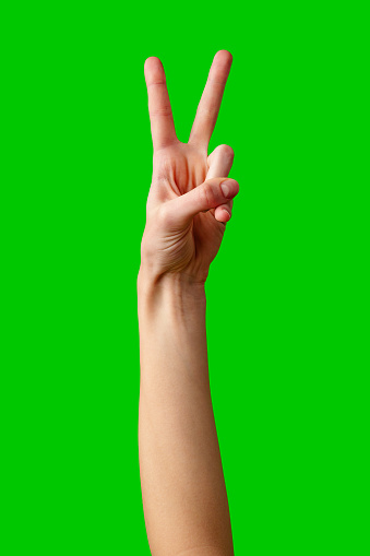 A single hand is raised against a bright green backdrop, with the index and middle fingers extended in a V-shape to form the universally recognized peace sign. The hand appears to belong to an adult, and the gesture conveys a message of peace and positivity.