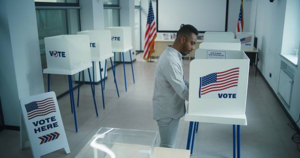 istock African American man votes in voting booth, then puts ballot in box 2149122431