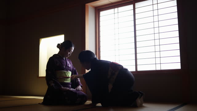 Female tourist in purple kimono learning manners of greetings from a senior instructor in dark Japanese tatami room - part 2 of 4