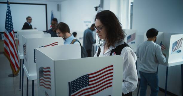 istock Woman in glasses votes in booth in polling station office 2149123551
