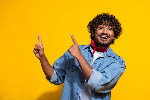 Photo portrait of attractive man point excited empty space dressed stylish denim clothes red scarf isolated on yellow color background.