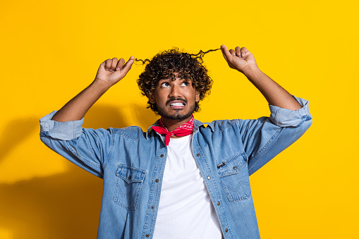 Photo portrait of nice young male hold look curly strands nervous wear trendy denim outfit red scarf isolated on yellow color background.