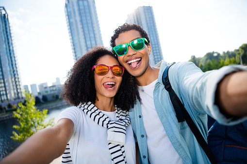 Selfie photographing young family couple wear casual outfit and sunglass stick tongue out for cadre with kyiv skyscrapers on background.