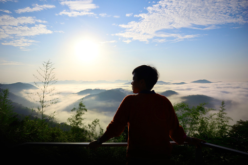 A person stands on a viewpoint in Phu Bo Bit Forest Park, Loei Province, Thailand. and watches the sunrise in the morning Miracle of nature, forest, hill, fog, standing, shadow, sunlight, mountain.