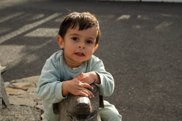 A young boy is sitting on a dog statue. He is smiling and has his hand on the statue