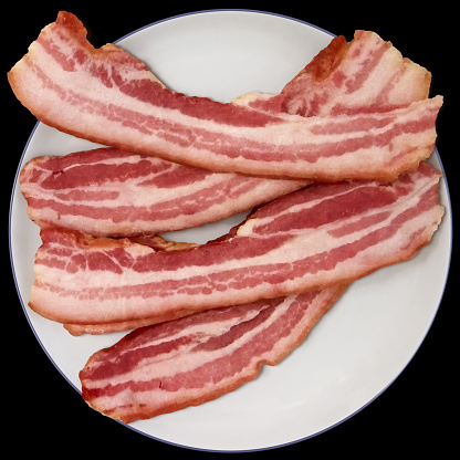Bunch of delicious meaty yummy gourmet Boiled Pork Bacon rashers, set on blue rimmed white ceramic plate, isolated on black background, high resolution stock photo.