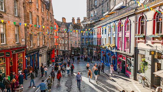 Aerial view of the famous colorful Victoria Street in the Old Town of Edinburgh, Scotland, England, Victoria Street in the United Kingdom, Victoria Street in the old town in Edinburgh Scotland England Crowds of tourists on the Royal Mile,harry potter city\n\nVictoria Street, a picturesque and winding cobblestone lane, is one of Edinburgh’s most iconic thoroughfares. Prior to its construction, access from the Grassmarket to the Lawnmarket was via the West Bow, a very steeply sloped and narrow lane. The new street was planned to demolish much of the old West Bow, and provide a broad sweeping link to the newly built George IV Bridge.