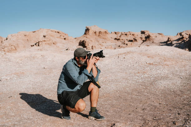 One man, handsome man sitting on the beach, taking pictures with camera.