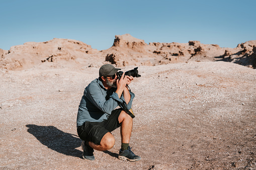 Mature male photographer kneeling to capture a perfect shot of the barren rocky landscape in the Atacama Desert, Chile, showcasing the beauty of Vallecito.