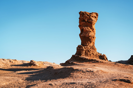 A distinct rock sculpture standing in Vallecito amidst the vast, tranquil Atacama Desert in Chile, under a clear blue sky.
