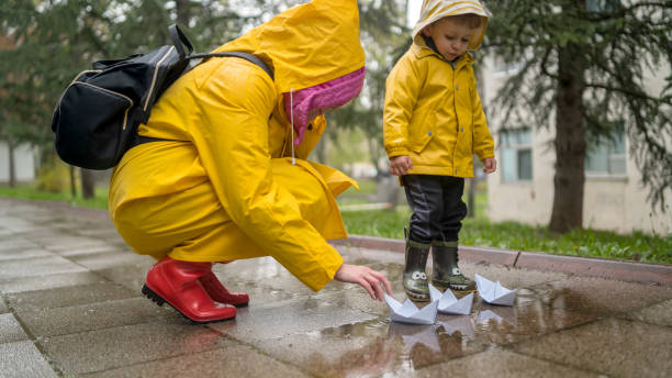 istock It's springtime. A small child in rubber boots jumps through puddles, plays and launches paper boats on the water. 2149128413