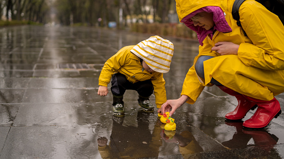 Little boy in raincoat and rubber boots playing in puddle