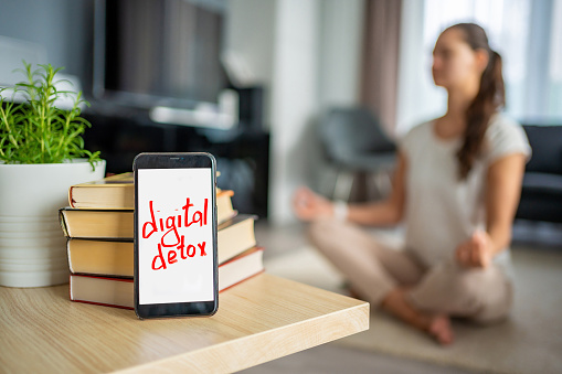 Digital detox concept. Smartphone with the text Digital Detox and woman meditating in the background. High quality photo