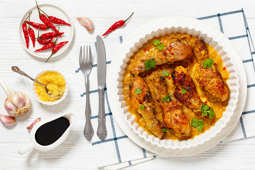 chicken drumsticks in crushed pineapple sauce in baking dish on white wooden table with ingredients and cutlery, horizontal view from above, flat lay